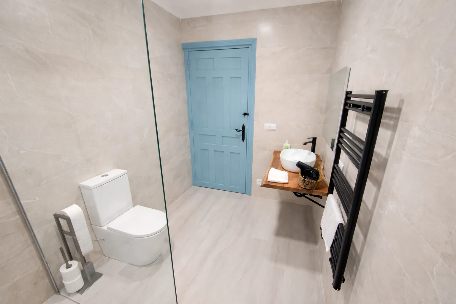Baño completo con ducha, lavabo sobre madera y toallero negro