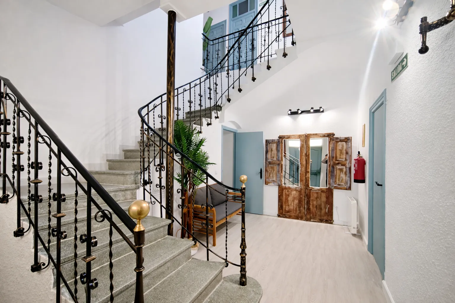 Entrada con escalera de forja, puertas de madera y asiento bajo la luz natural