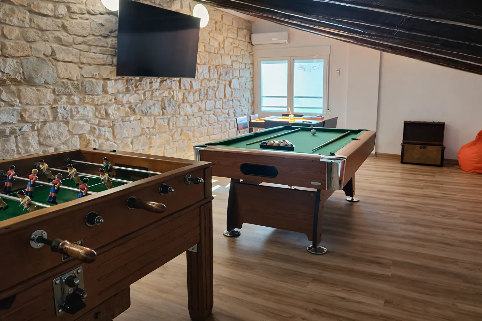 Sala de juegos con futbolín, billar y pared de piedra